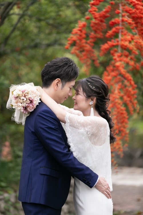 赤い実をつけた枝の下で額を寄せ合う新郎新婦。花嫁はレースのボレロと白いドレス、手には淡いピンクのブーケを持った結婚写真