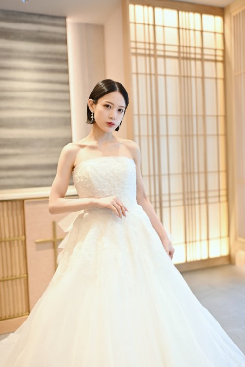 木の格子の壁の前でビスチェのチュールのウェディングドレスを着て立つ花嫁を縦位置でとらえた一枚。東京駅店のスタジオで撮る洋装前撮りのドレス写真