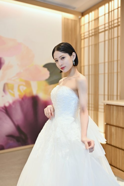 紫と桃色の花のアートウォールを背にビスチェのチュールのウェディングドレスの裾を持つ花嫁を縦位置でとらえた一枚。東京駅店のスタジオで撮る洋装前撮りのドレス写真