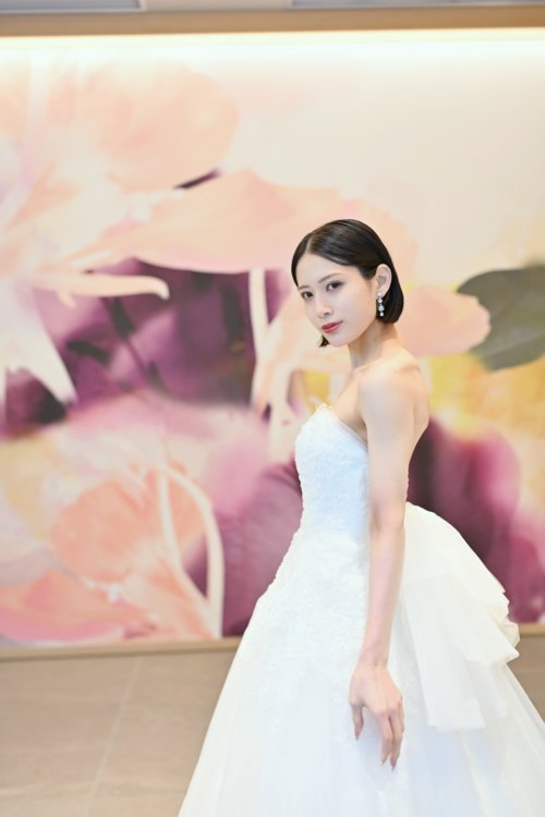紫と桃色の花のアートウォールの前でビスチェのチュールのウェディングドレスを着て横を向く花嫁を縦位置でとらえた一枚。洋装前撮りで選べるウェディングドレスの衣装写真