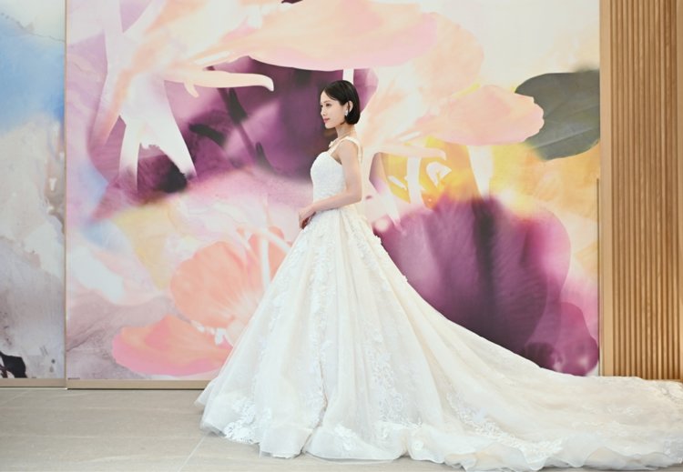 紫と桃色の花のアートウォールを背にレースのトレーンを広げて立つウェディングドレスの花嫁。東京駅店のスタジオで撮る洋装前撮りのドレス写真