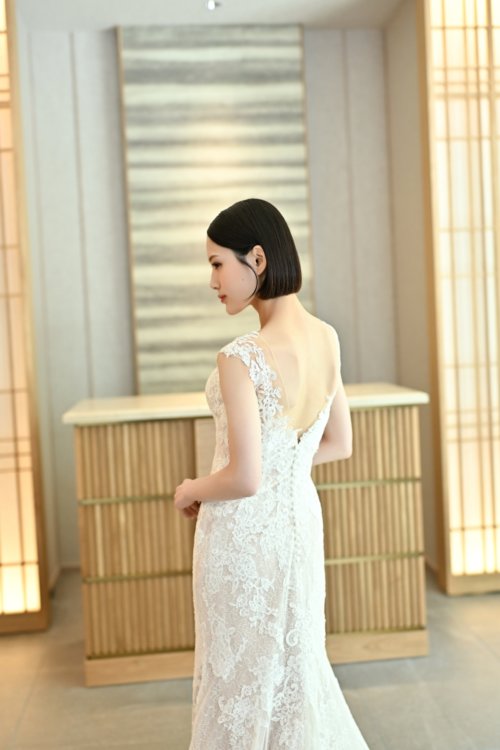 木の格子の壁の前で背中の開いたレースのウェディングドレスを着て横を向く花嫁を縦位置でとらえた一枚。東京駅店のスタジオで撮る洋装前撮りのバックスタイル