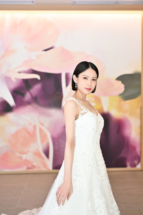 紫と桃色の花のアートウォールの前でレースのウェディングドレスを着て微笑む花嫁を縦位置でとらえた一枚。東京駅店のスタジオで撮る洋装前撮りのドレス写真