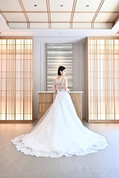 障子の部屋でレースのAラインのウェディングドレスのトレーンを広げて立つ花嫁の後ろ姿を縦位置でとらえた一枚。東京駅店のスタジオで撮る洋装前撮りのバックスタイル
