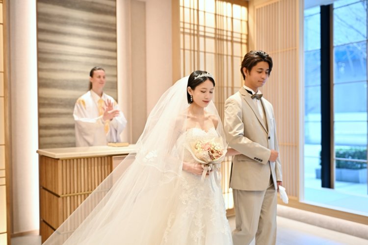 祭壇の前で牧師と向かい合うベージュのスーツの新郎とベールのウェディングドレスの花嫁。東京駅店のスタジオで撮るチャペルフォトの一場面