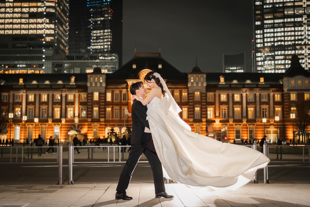 夜の東京駅丸の内駅舎を背景に、花婿が花嫁を抱き寄せドレスの裾がなびくダンスシーン