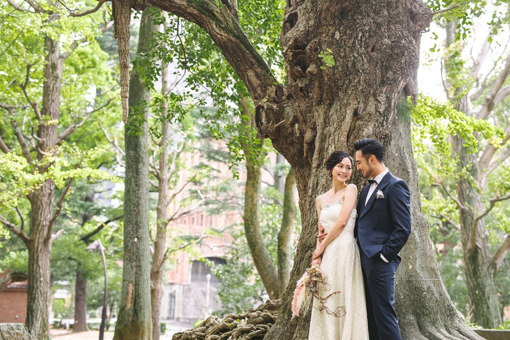 日比谷公園でのウェディングドレス前撮り、豊かなグリーンと噴水を背景にドレスが清潔感よく映える美しい一枚