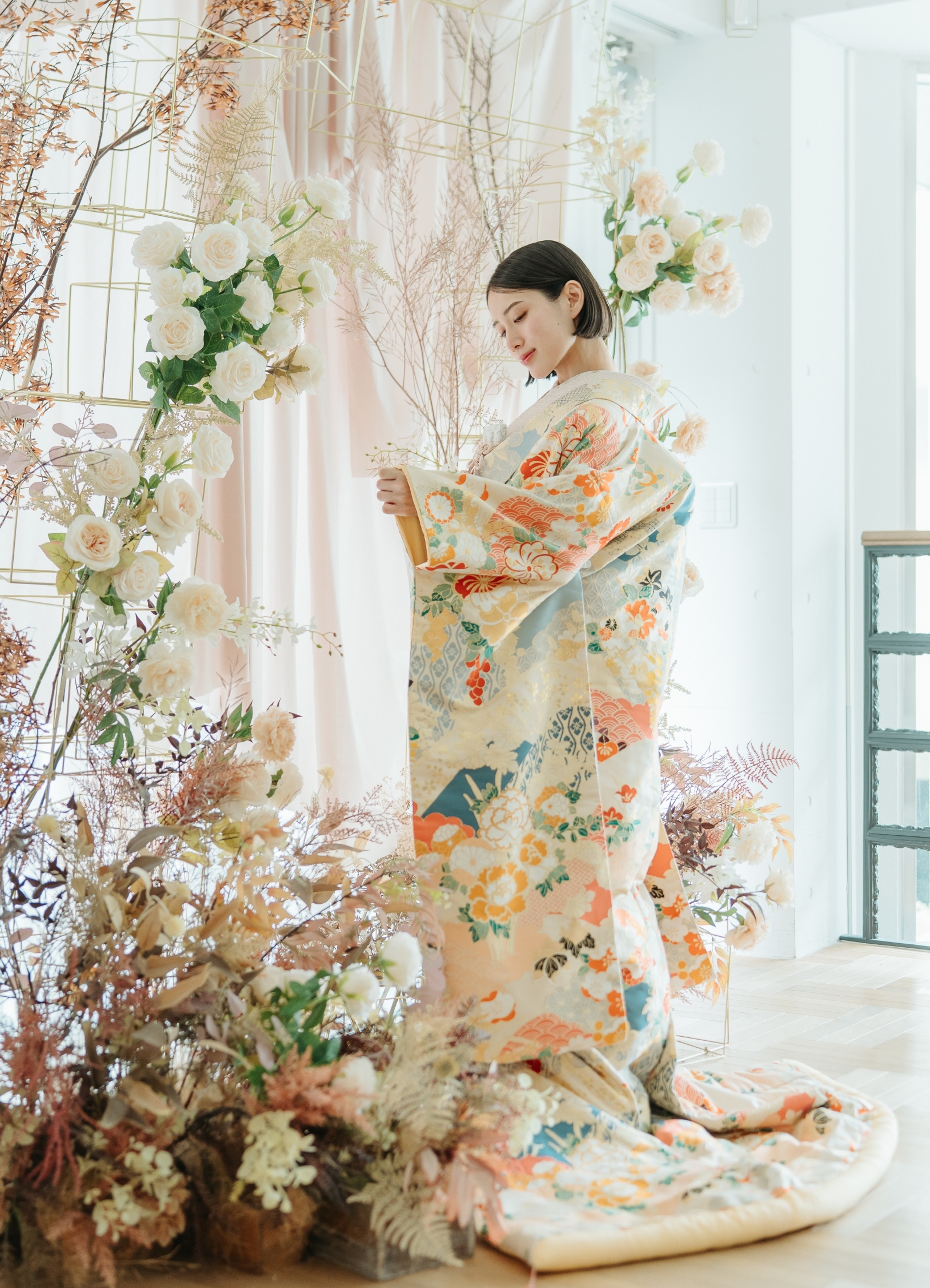 白地に朱の花柄が映える色打掛をまとい、ドライフラワーの装花に囲まれたスタジオに佇む花嫁の和装前撮り（東京駅店）
