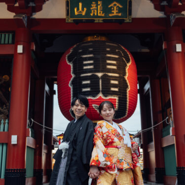 浅草寺 雷門の大提灯の下で手をつなぎ、笑顔を向ける黒紋付袴の新郎と色打掛の花嫁。浅草の和装前撮りを象徴する一枚