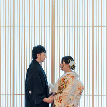 白いカーテンの前でブーケを持って立つウェディングドレスの花嫁を縦位置でとらえた一枚。スタジオで撮る洋装前撮りのブライダルポートレート