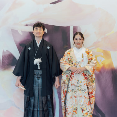 縦格子の障子の前で白い和傘を差す黒紋付袴の新郎と白無垢の花嫁を縦位置でとらえた一枚。東京駅店のスタジオで撮る和装前撮り