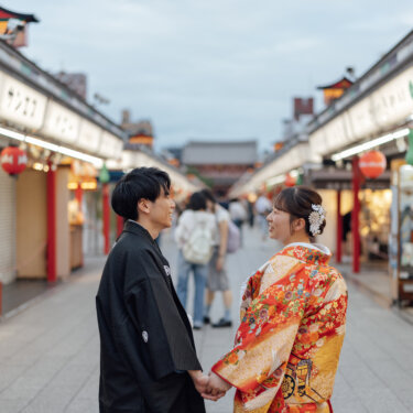 提灯が並ぶ仲見世通りで手をつないで見つめ合い、笑い合う羽織袴の新郎と色打掛の花嫁。浅草らしい活気の中の和装前撮り