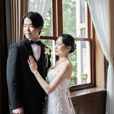 旧古河邸にて、窓辺で新郎の胸に手を添えて寄り添うレースのウェディングドレスの花嫁。遠くを見つめる新郎との大人っぽい結婚写真