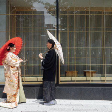 青いアートウォールの前で袖を広げて振り返る白無垢の花嫁を縦位置でとらえた一枚。東京駅店のスタジオで撮る和装前撮りのブライダルポートレート