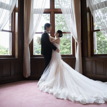ピンクの絨毯にトレーンを大きく広げ、窓辺で抱き合う新郎新婦のシルエット。洋館で撮るロマンチックな結婚写真