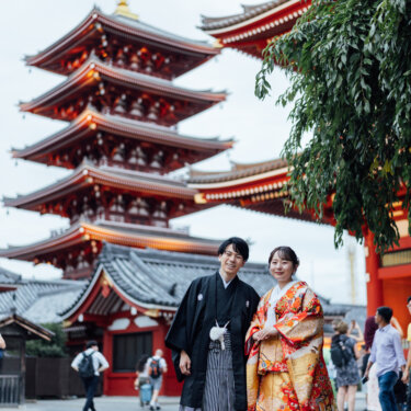 朱色の五重塔の前に並んで立つ羽織袴の新郎と赤い色打掛の花嫁の全身ショット。浅草寺で撮るロケーションフォトの定番構図