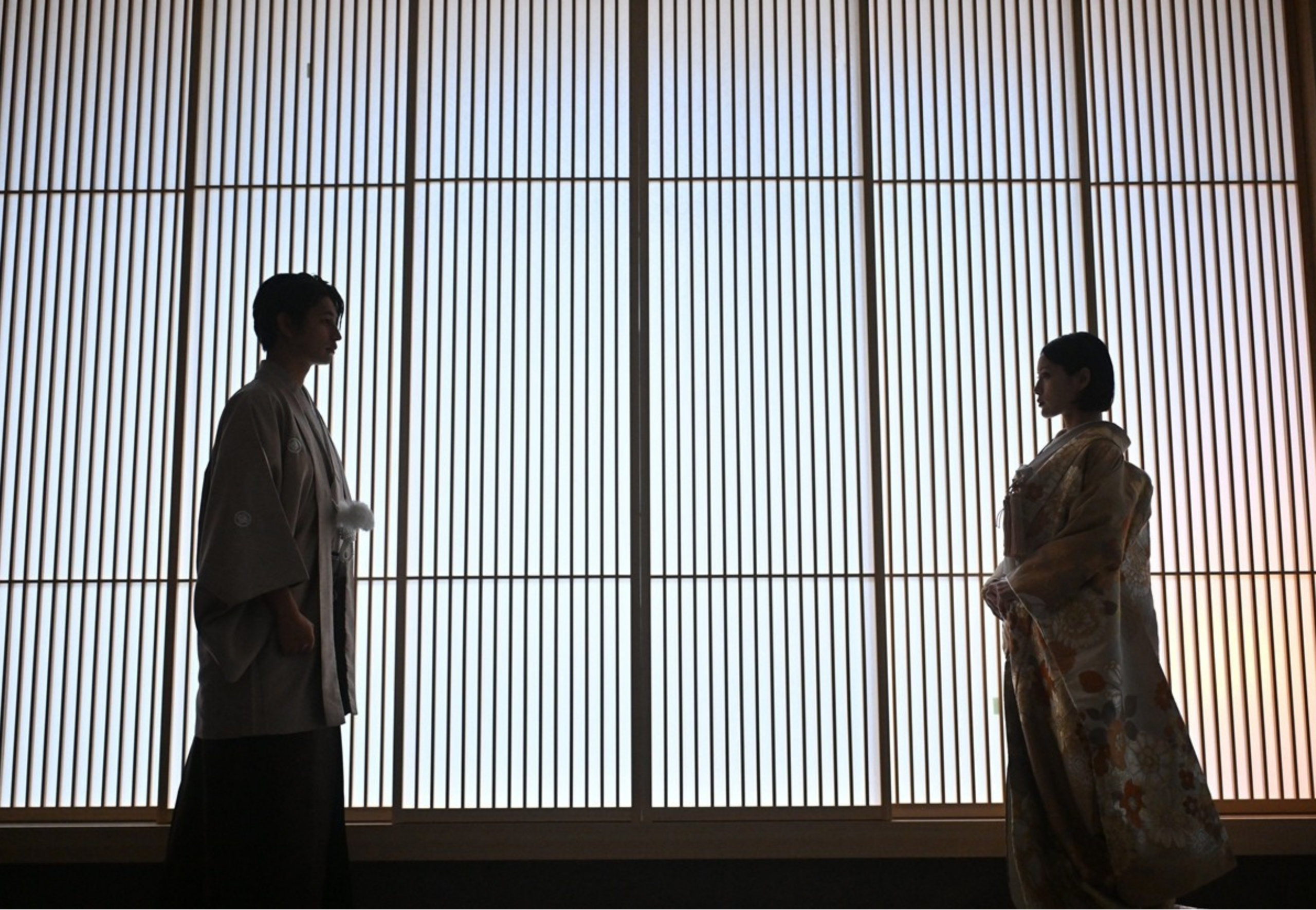 大きな格子窓の光を背に、和装姿でシルエットになって向かい合う新郎新婦。映画のワンシーンのようなムービー＆フォトプランの一場面