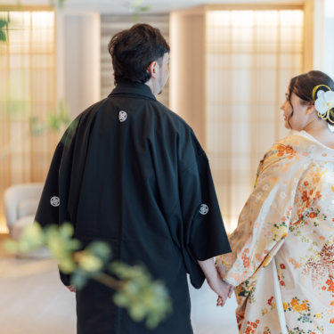 赤い和傘を肩にかけて振り返って笑う白無垢の花嫁を縦位置でとらえた一枚。和傘を使った和装前撮りのポーズ