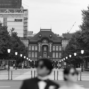 行幸通りの先に東京駅丸の内駅舎が見えるモノクロ写真で、手前にサングラス姿の新郎新婦をぼかして写したおしゃれな結婚写真