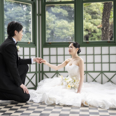市松模様の床に座る花嫁の手を取り、ひざまずく新郎。緑の窓枠のサンルームで撮るプロポーズのようなフォトウェディング