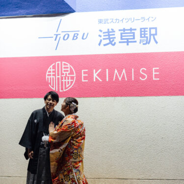 東武スカイツリーラインの浅草駅の案内サインの前で、笑いながら向き合う羽織袴の新郎と色打掛の花嫁。遊び心ある和装前撮りのポーズ