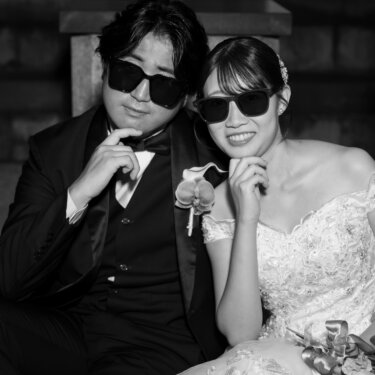 石造りのアーチに腰かけ、おそろいのサングラスで頬杖をつく新郎新婦のモノクロ写真。遊び心のあるポーズで撮るおしゃれな結婚写真