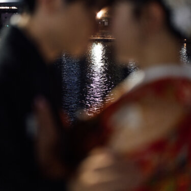 夜の川面に映る光をぼかして、おでこを寄せ合う羽織袴の新郎と色打掛の花嫁をとらえた映画風の前撮り写真