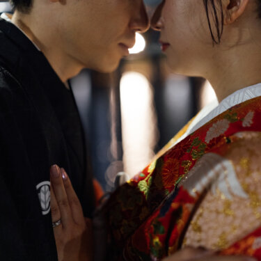 黒紋付の胸元に手を添え、目を閉じて顔を寄せ合う新郎と色打掛の花嫁。夜の街灯に照らされたしっとりとした和装の結婚写真