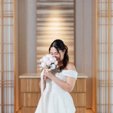 青いイルミネーションの前でブーケを高く掲げるウェディングドレスの花嫁と新郎を縦位置でとらえた一枚。イルミネーションで撮るナイトフォト前撮り