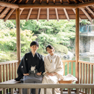 目白庭園の東屋のベンチに並んで腰かけて微笑む白無垢の花嫁と黒紋付の新郎。座って撮る和装の結婚写真
