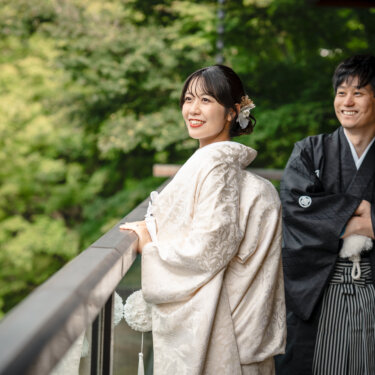 緑を背に回廊の手すりにもたれて笑い合う白無垢の花嫁と黒紋付の新郎。目白庭園の和装ロケーションフォト