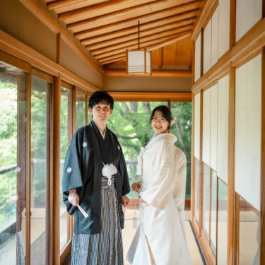 和風の照明が並ぶガラス張りの回廊で向かい合う新郎新婦。白無垢の裾を引いた屋内の和装前撮り
