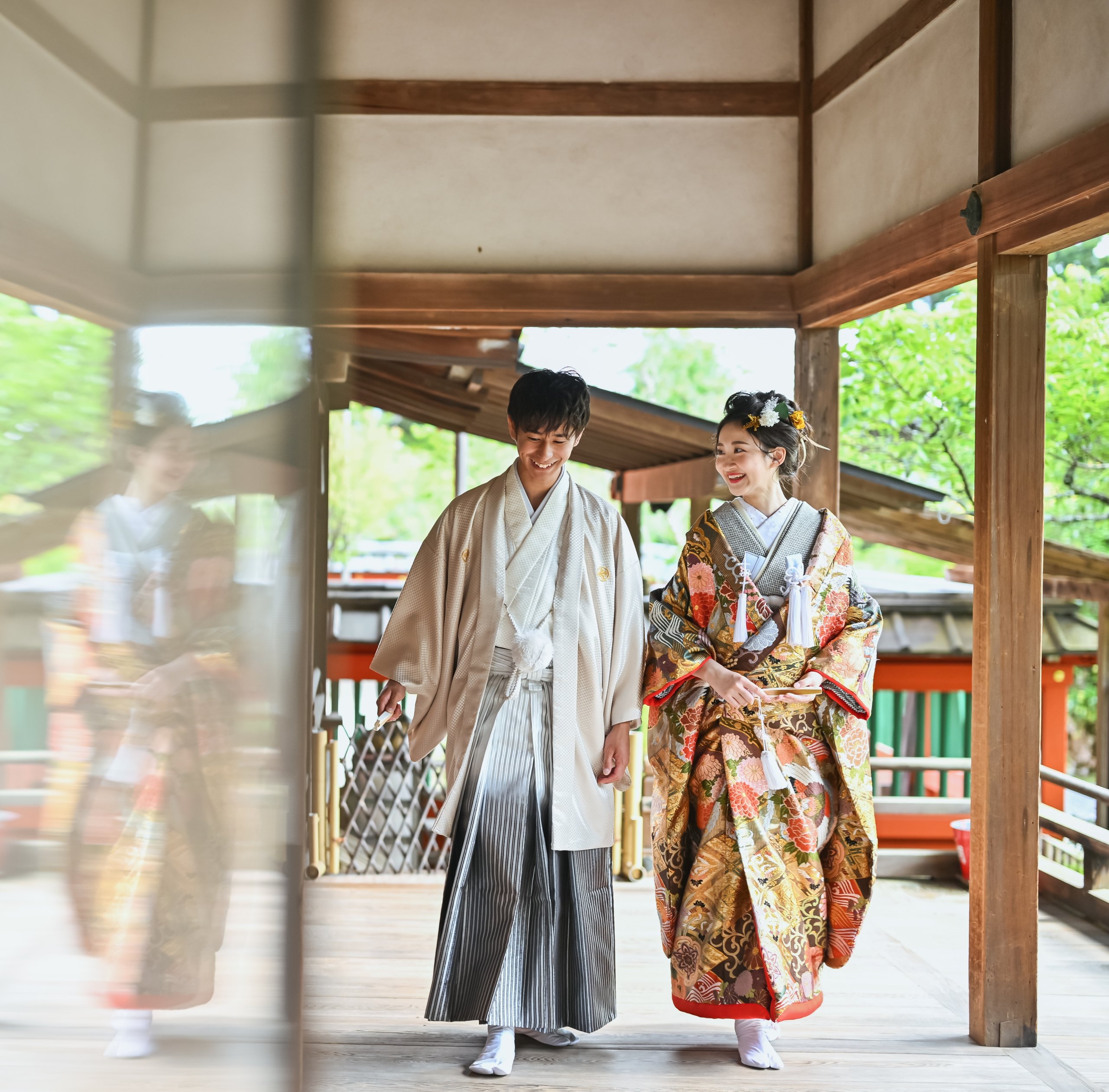 神社の回廊を並んで歩く、金茶の色打掛の花嫁と白い紋付羽織袴の新郎の和装ロケーションフォト