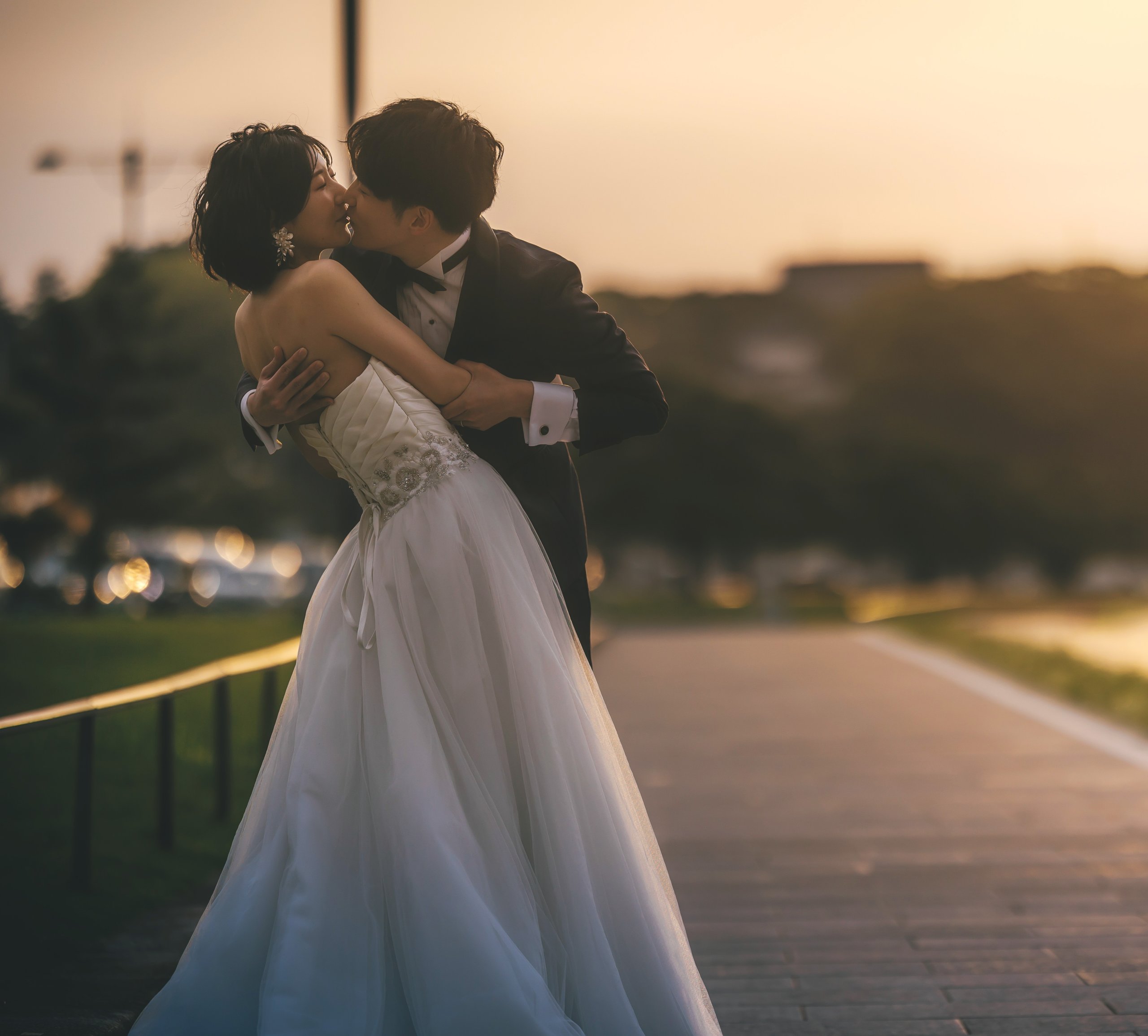 夕暮れの遊歩道で抱き合う新郎新婦。裾がブルーにグラデーションするウェディングドレスのサンセットフォト