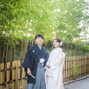 竹林と竹垣が続く小道に並んで立つ紋付袴の新郎と白無垢の花嫁。緑に映える和装フォトウェディング