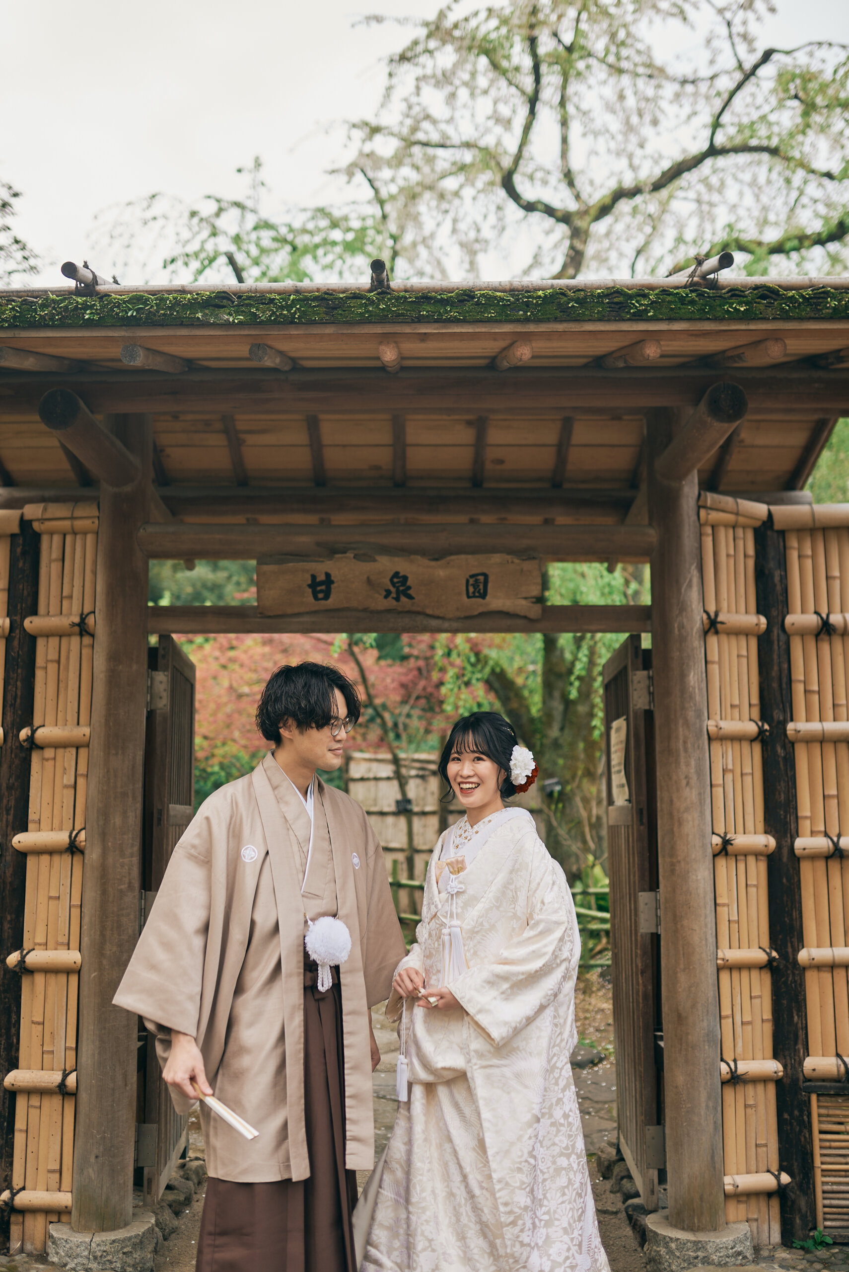 甘泉園公園の竹垣の門の前に並ぶ白無垢姿の新婦と紋付袴姿の新郎