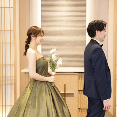 障子風の和モダンなスタジオで、背中合わせに立つネイビーのタキシードの新郎とカーキのカラードレスの花嫁。ファーストミート直前の洋装前撮り
