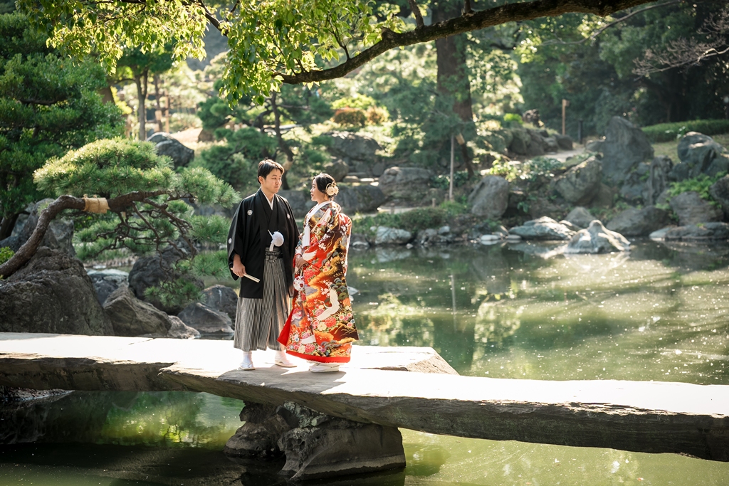 清澄庭園の池にかかる一枚石の石橋の上で寄り添う色打掛の花嫁と紋付袴の新郎の和装前撮り