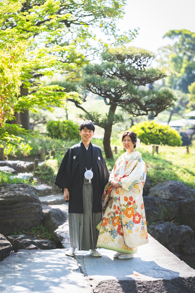清澄庭園の磯渡りの石の上に並んで立つ色打掛の花嫁と紋付袴の新郎。池の中を歩いて撮る和装ロケーションフォト