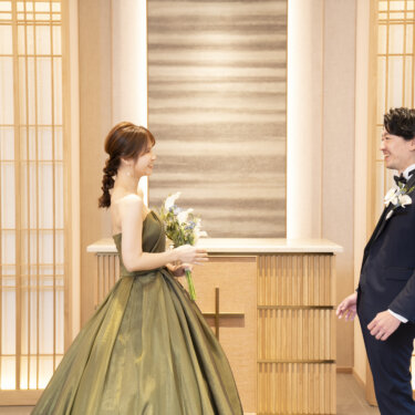 初めてドレス姿を見た新郎と、白いブーケを持って微笑む三つ編みの花嫁が向かい合う瞬間。和モダンなスタジオでのファーストミートの前撮り