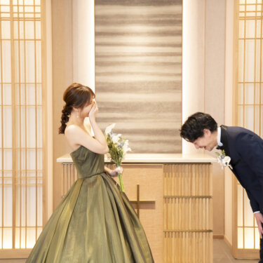 花嫁のドレス姿に感激して深くお辞儀をするタキシードの新郎と、口元を押さえて笑う花嫁。東京駅店のスタジオフォトで撮るファーストミート