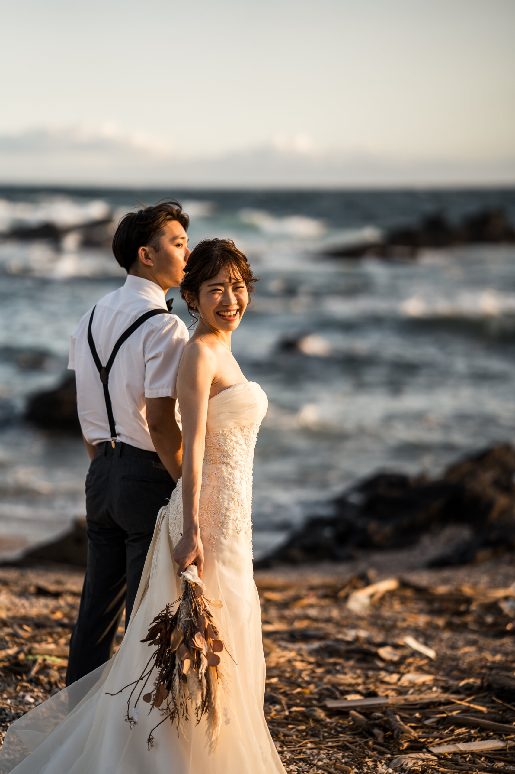 城ヶ島の海に沈む夕日を背景に寄り添う新郎新婦。オレンジ色の空が広がるサンセットのウェディングフォト