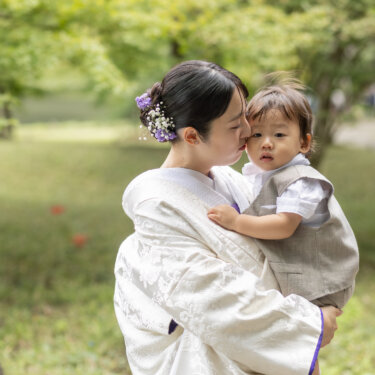 緑の芝生の庭で男の子を抱き、ほおにキスする白無垢の花嫁。小石川後楽園で撮る家族写真入りの和装前撮り