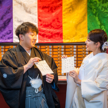 おみくじの結果を見せ合いながら笑い合う紋付袴の新郎と白無垢の花嫁。浅草寺での遊び心ある和装前撮り