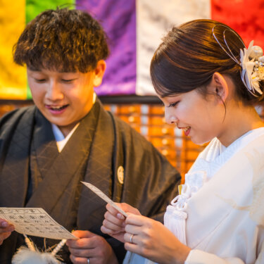 おみくじを手に、うれしそうに読み合う紋付袴の新郎と白無垢の花嫁のアップ。笑顔あふれる和装ロケーションフォト