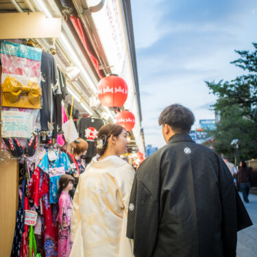 浅草の仲見世通りで、土産物店の軒先をのぞきながら歩く白無垢の花嫁と紋付袴の新郎の後ろ姿の結婚写真