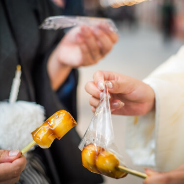 紋付袴と白無垢のおふたりがみたらし団子を手に持つ手元のアップ。浅草の食べ歩きを楽しむ前撮りアイテム