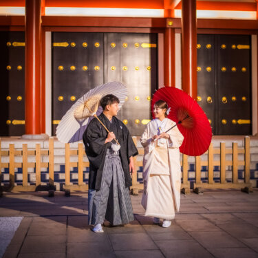 ライトアップされた浅草寺の朱塗りの門前で、和傘を手に並んで歩く紋付袴と白無垢のおふたりの和装前撮り