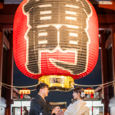 夜の浅草寺で大提灯の下に立ち、白無垢の花嫁に指輪を贈る紋付袴の新郎。夜景が美しい和装フォトウェディング
