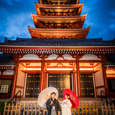 夜空に浮かぶライトアップされた浅草寺の五重塔の前で、和傘を持って並ぶ紋付袴の新郎と白無垢の花嫁の結婚写真